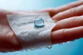 Photographie macro montrant une goutte d'eau glissant sur un bandage étroitement enroulé autour d'une main, indiquant les propriétés résistantes à l'eau du bandage, en arrière-plan flou avec un éclairage dramatique.