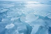 Photographie en gros plan d'une épaisse couche de glace blanche scintillante, accentuée par des nuances de bleu, s'étendant sur un lac gelé, mise au point nette, éclairage ambiant.